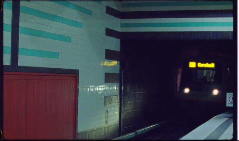 A modern subway train with white red and blue accents coming to a stop at a stationthe footage is shot in a grainy vintage film style featuring a filmsupply watermark across the center