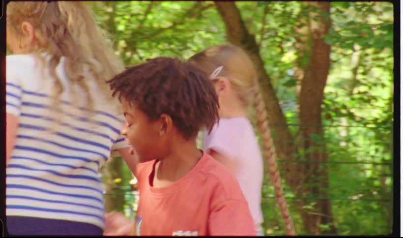 A group of friends including boys and girls play together in a circle on a sunny day in a park with green trees in the background