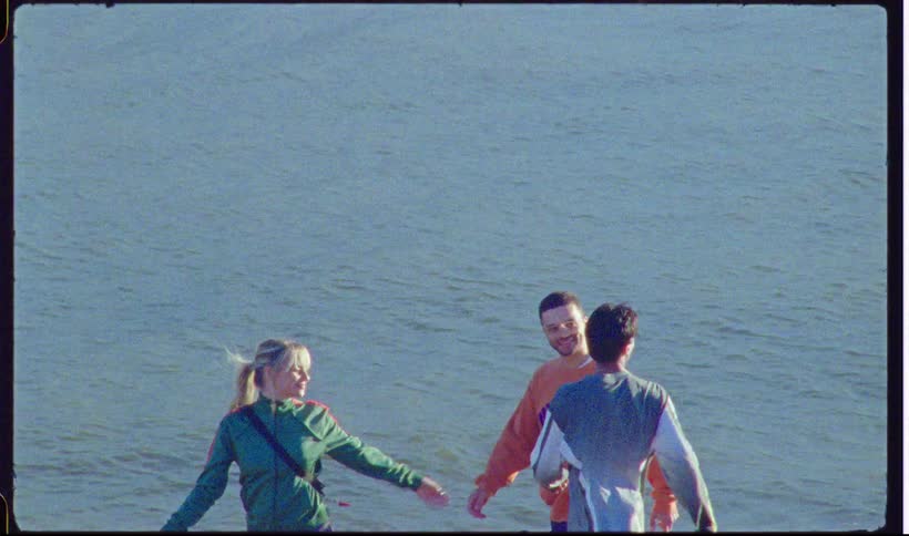 Three young people walk and talk along a sandy shoreline by the ocean