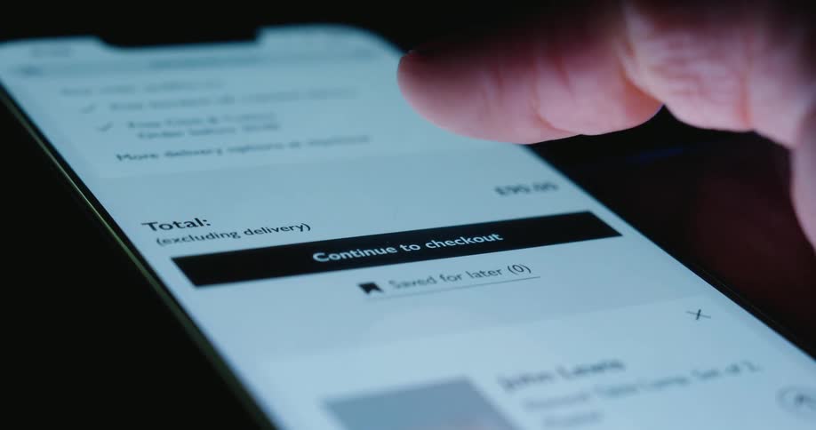 In a dark background a persons thumb is scrolling on a smart phone appearing to be checking out on an app