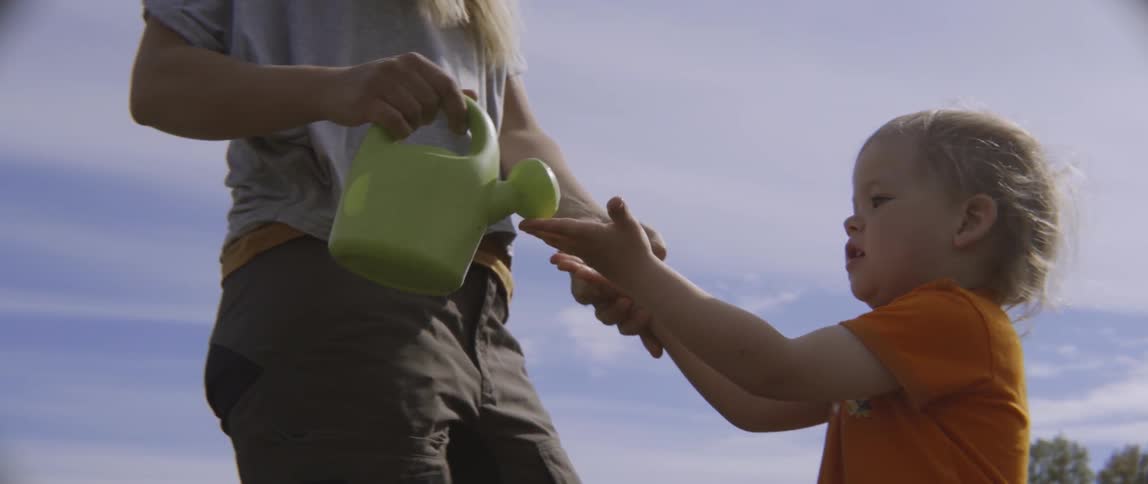 A toddler boy and his mother are playing with a toy watering can outdoors