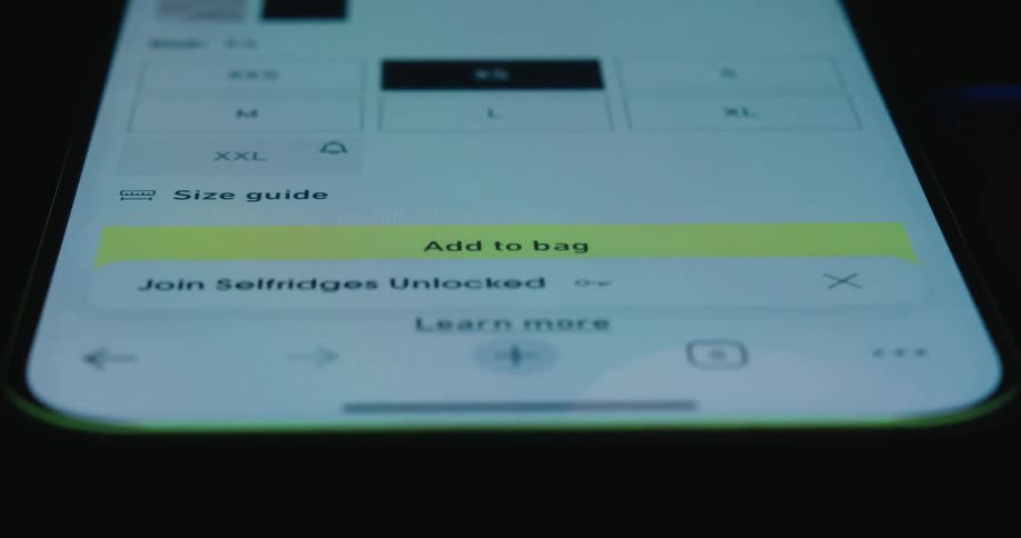 A close view of a person using a finger to tap the add to bag button on a shopping website displayed on a mobile phone screen