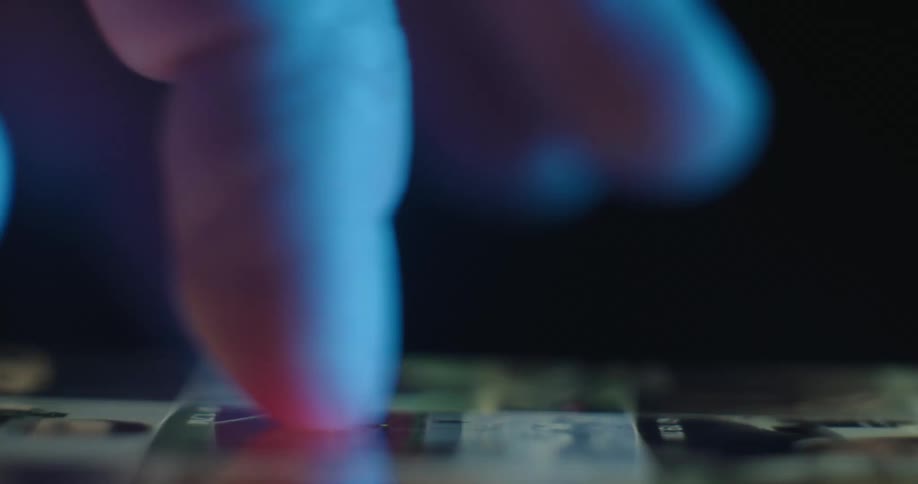 A close view from the side shows a finger scrolling through various colorful images on a mobile phone screen in a dark room with blue light