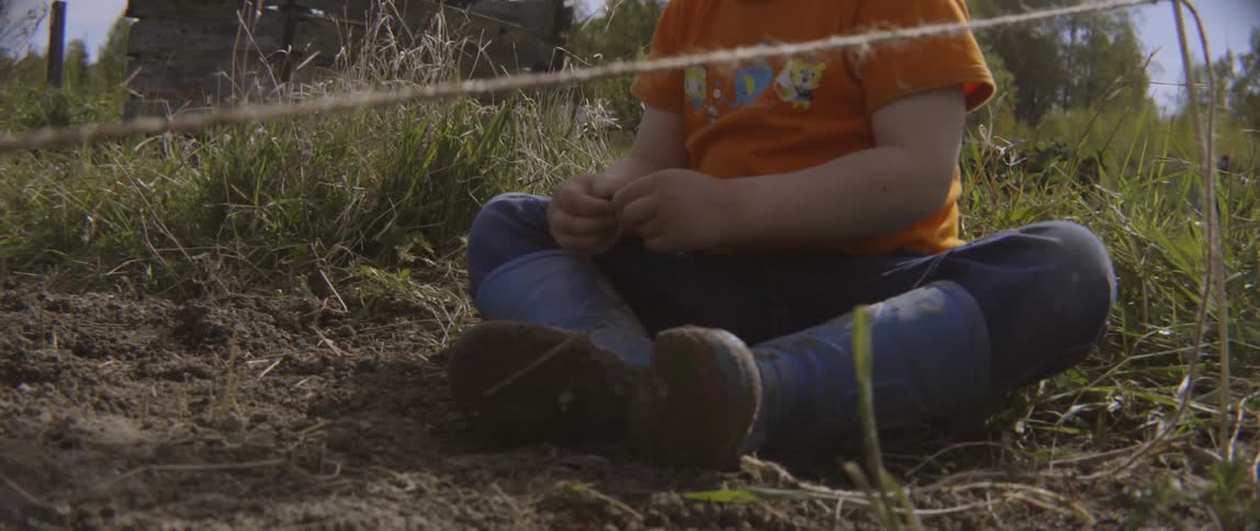 Young boy sitting on the ground playing in the dirt during summertime outdoors.