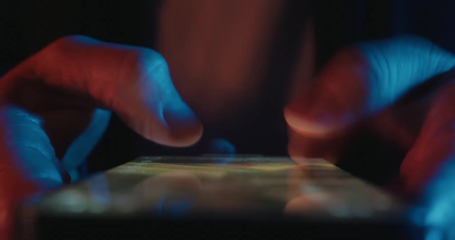 A closeup shot of a persons hands using their thumbs to rapidly scroll through a social media or photo feed on a smartphone the scene is set in a dark environment with dramatic blue and orange lighting reflecting off the screen and the persons skin