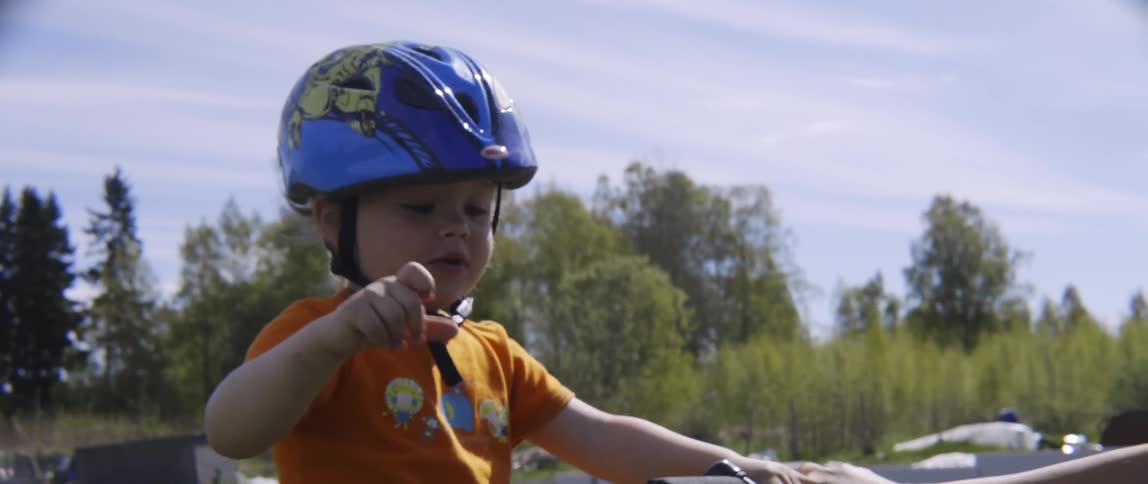 A young toddler boy wearing a safety helmet sits on a bicycle outdoors in nature.