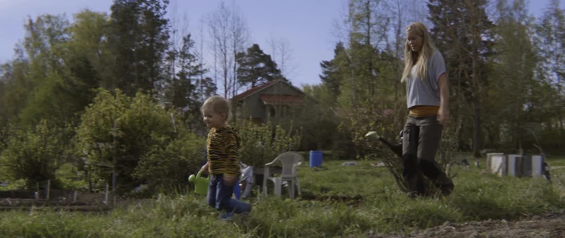 Woman and toddler boy carrying watering cans outside on sunny day