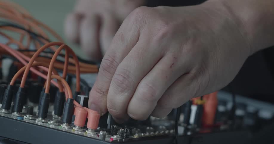 Mans hands moving dials and pressing buttons on a soundboard