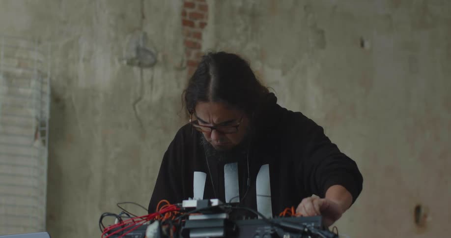 A focused man adjusting electronic equipment with wires on a table inside a worn industrial room