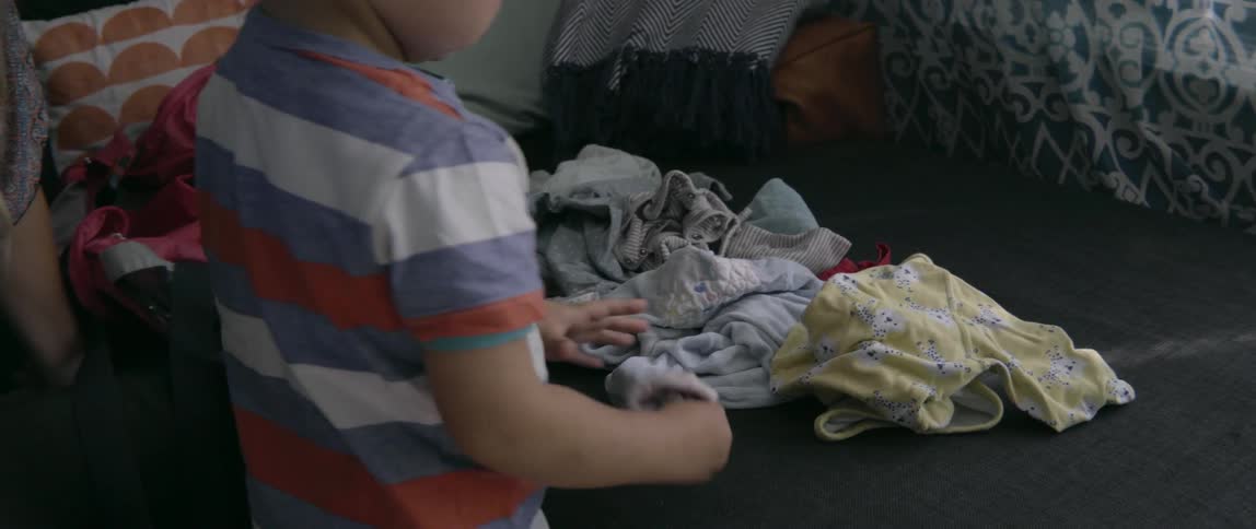 A toddler boy playing with clean laundry while sitting in a bright living room.