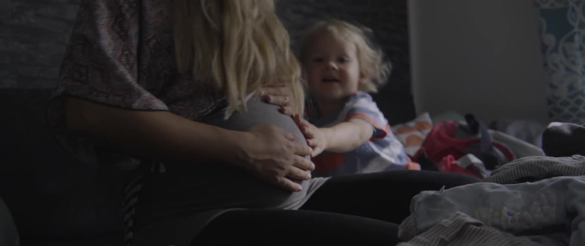 Pregnant mother and toddler boy bonding while touching her belly in a sunny home.
