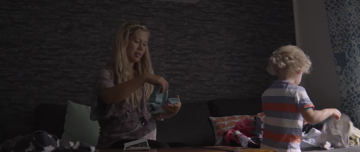 Young child assisting his mother with folding clothes in a natural home setting.