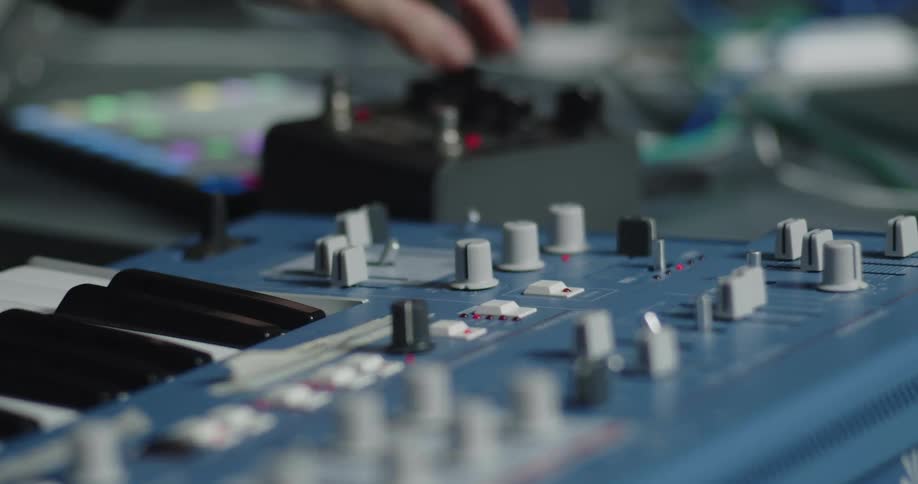 A mans hands operating musical equipment inside a studio as he adjusts the knobs