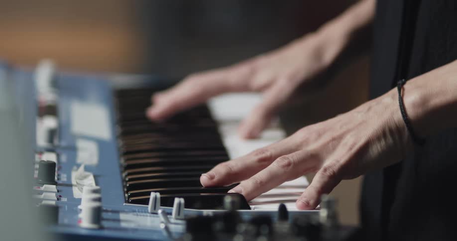 Hands playing keys on an electronic synthesizer