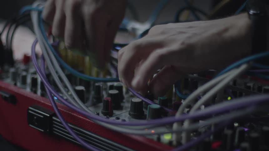 Mans hands moving cables near dials on a soundboard
