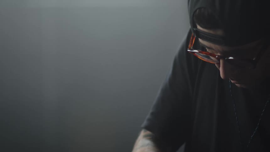 A close view from the side shows a person wearing a black shirt and glasses as they look down while working in a dark room with soft light