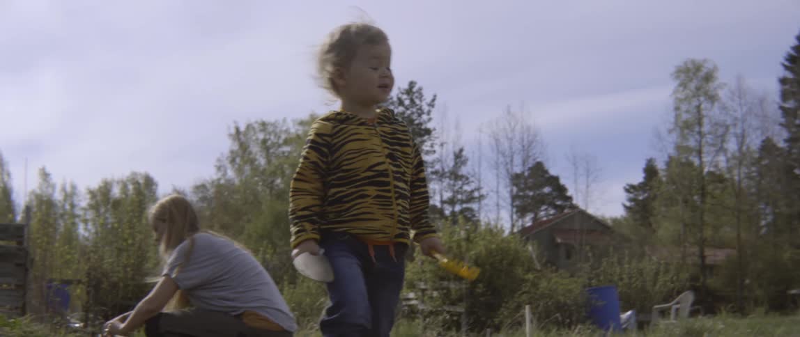 A child carrying a toy shovel walks in a garden