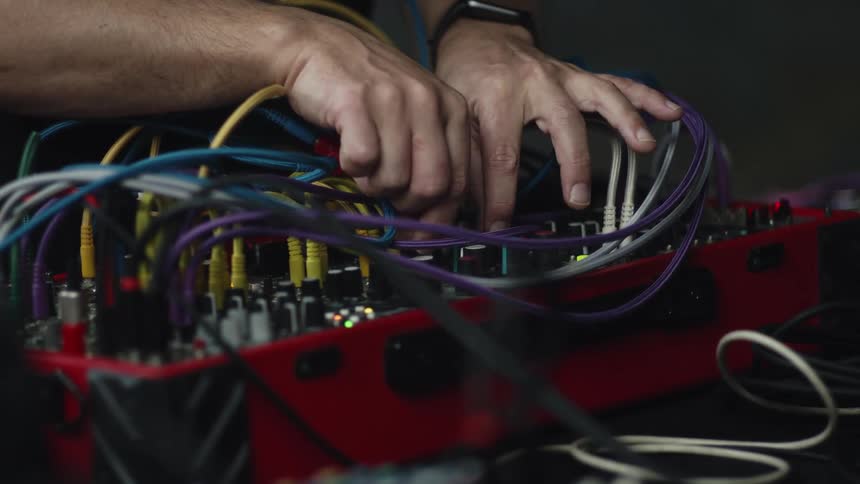 A musician adjusts patch cables and knobs on a modular synthesizer system