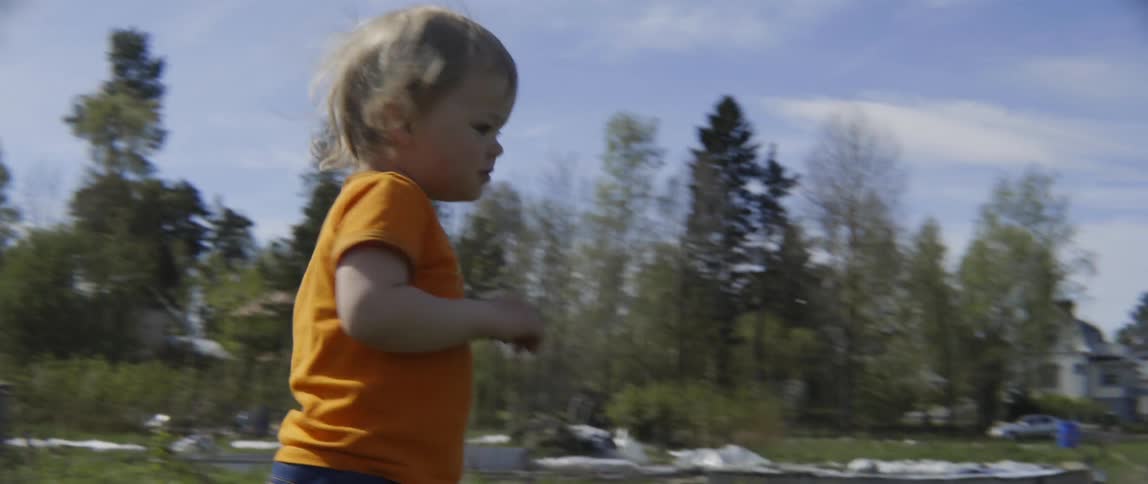 Small toddler boy walking toward the camera while playing outside in a natural environment.