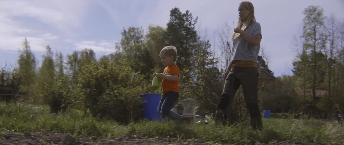 A woman and young boy walking together through a lush green grassy area.