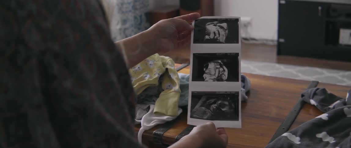 Woman sitting on a sofa while viewing sonogram pictures in a living space.