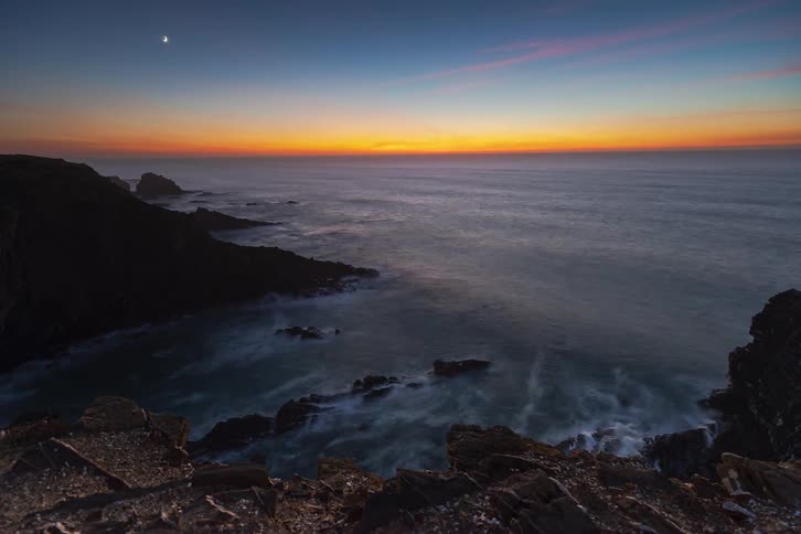 Glowing horizon after sunset over the ocean with waves hitting rocks along the coast