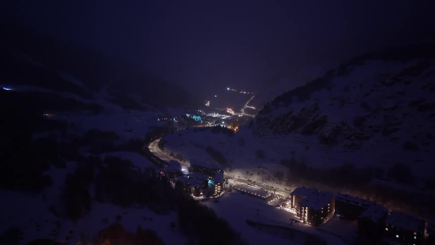 Illuminated village at night in a snowcovered mountain valley with a winding road