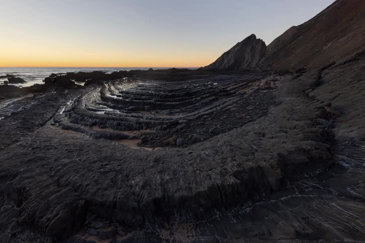 Curved layered rock formation on the coast with the ocean in the background at nightfall