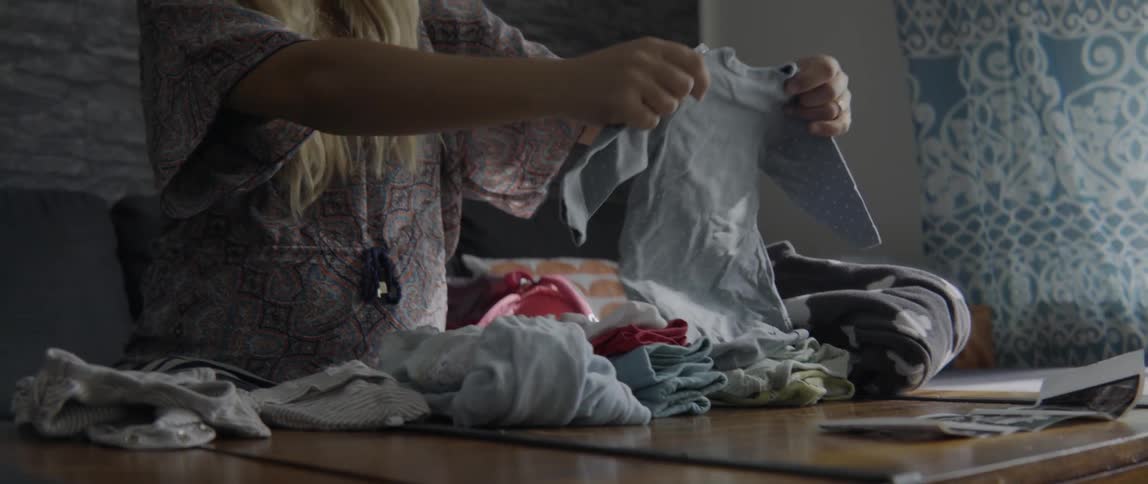 Close up of a woman organizing fresh clothing while sitting at a wooden table.