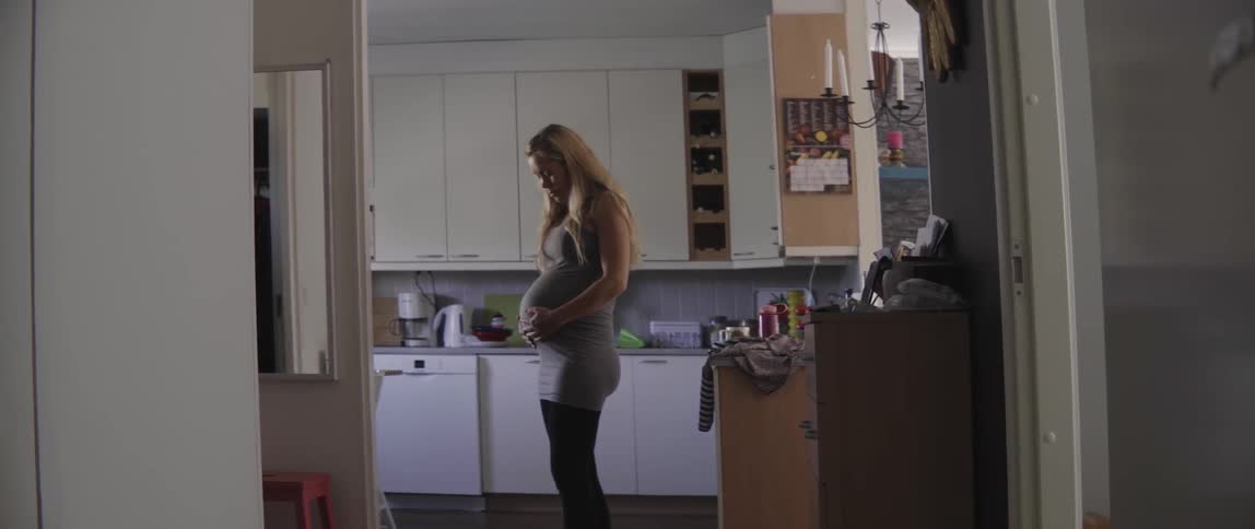 A pregnant woman standing in a kitchen rubs her belly
