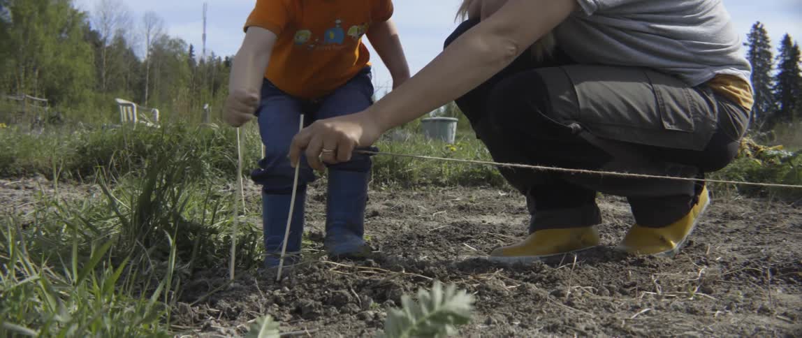 A woman crouches down as a boy puts a stake in the ground