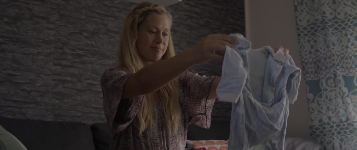 Expectant mother folding clean baby clothes while preparing for her new arrival at home.