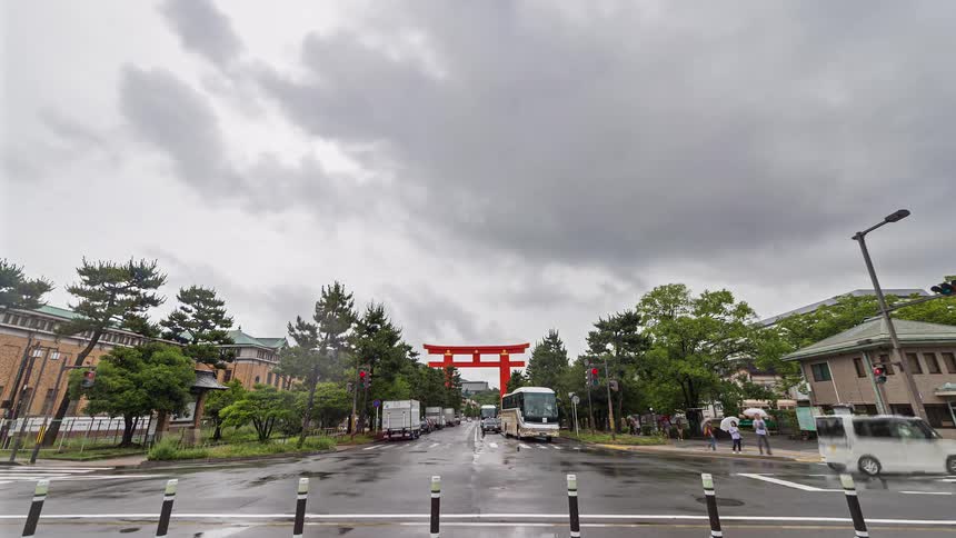 Vehicular and pedestrian traffic moves through an intersection near a torii arch on a cloudy day