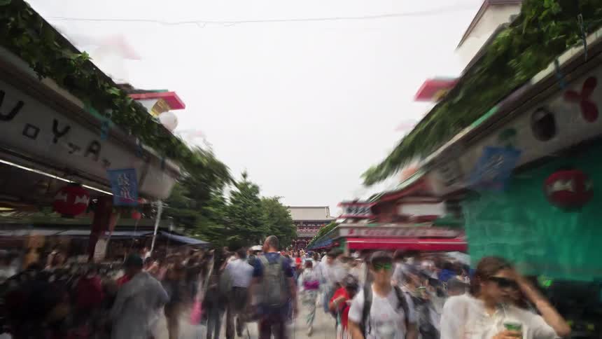Visitors move through the courtyard toward a grand red temple gate its ornate traditional architecture standing prominently against a pale sky
