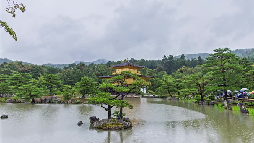 Golden temple surrounded by a lake and trees in a japanese garden with mountains in the background