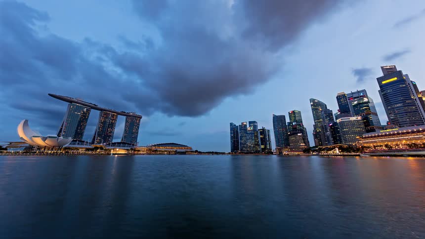 Watercraft pass through the harbor near a city as day turns into night