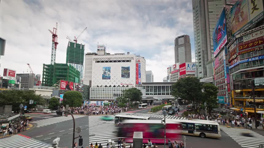 Many pedestrians cross a busy urban intersection as construction cranes build a high rise nearby