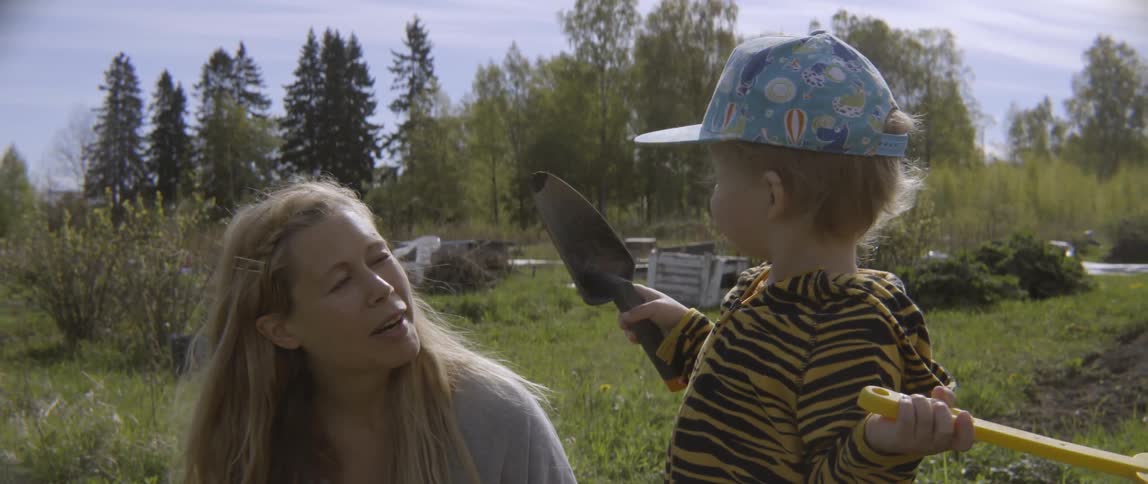 Woman talks to toddler boy holding a shovel outside on sunny day