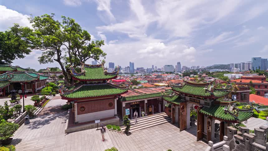 People move through a gate in an area with traditional asian architecture in a city on a cloudy summer day