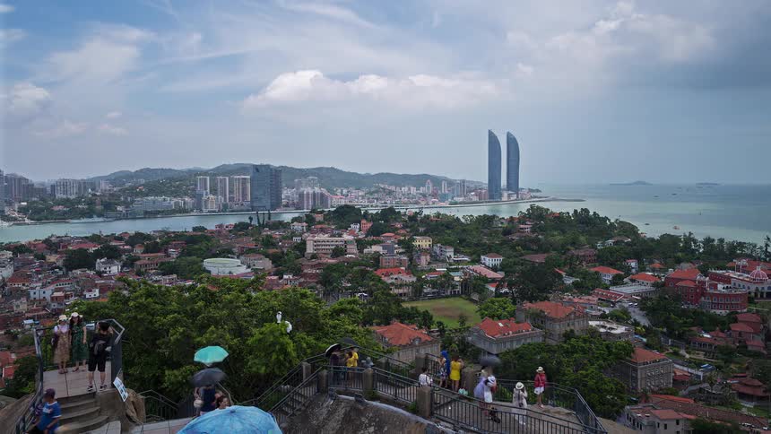 A group of tourists walking up a staircase at a tourist site with the city skyline in the background at midday