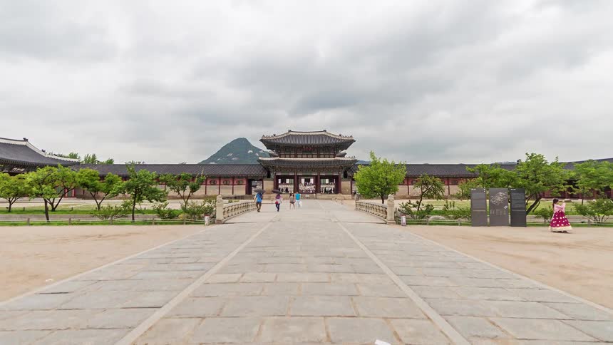 A sequence of shots shows the ornate gates and grand halls of gyeongbokgung palace in seoul as people walk through the stone courtyards under a grey sky with mountains in the distance