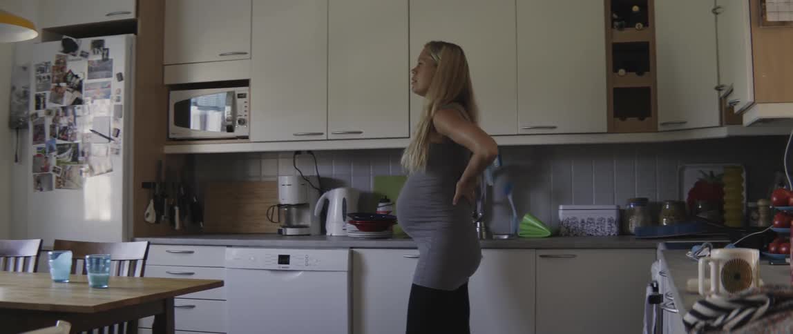 Pregnant woman standing in her kitchen with her hands on her lower back