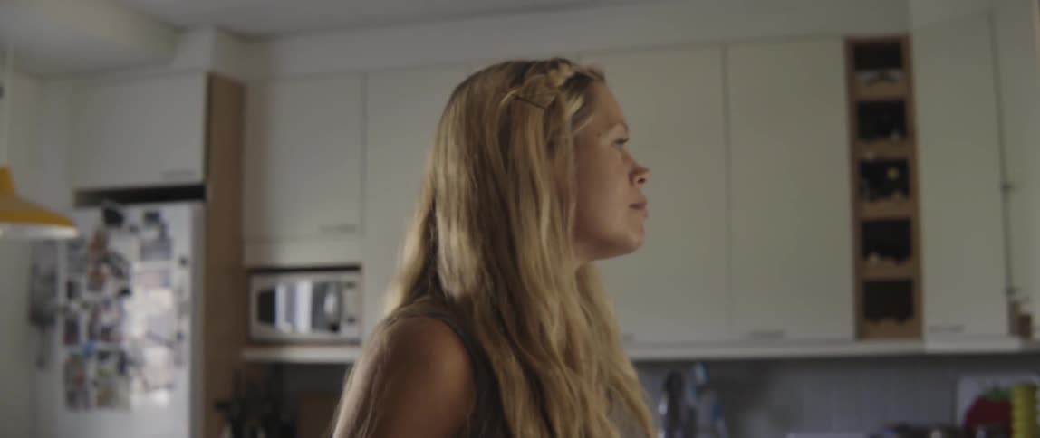 Young pregnant woman standing in a sunny kitchen while touching her baby bump tenderly.