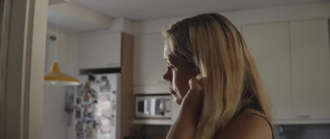 Close up of a young blonde woman touching her ear while at home.