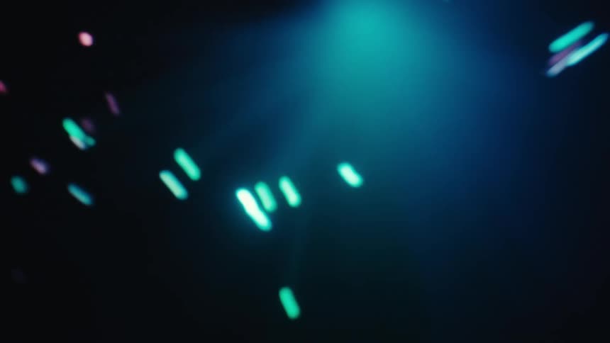Blue and purple light particles float and move across a dark background while a soft blue glow shines from above