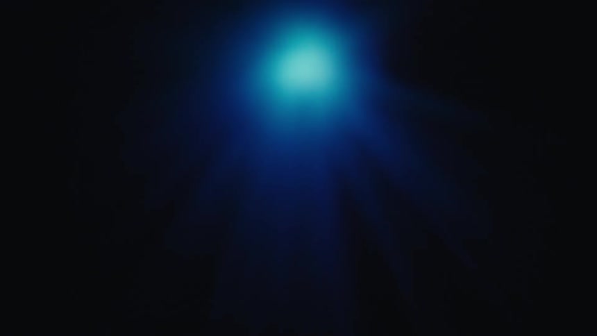 A bright blue orb of light glows in the center of a dark space emitting soft rays of light outward while small purple bokeh spots linger in the corners of the frame before fading into the deep blue atmosphere