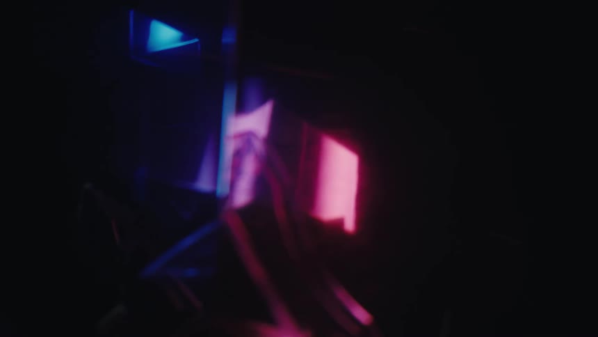 Geometric shapes illuminated in blue and pink creating reflections in a dark environment