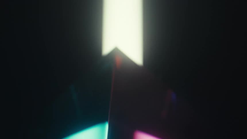 A close view of a glass prism rotates as bright beams of yellow and blue light pass through the facets to create colorful reflections against a dark background