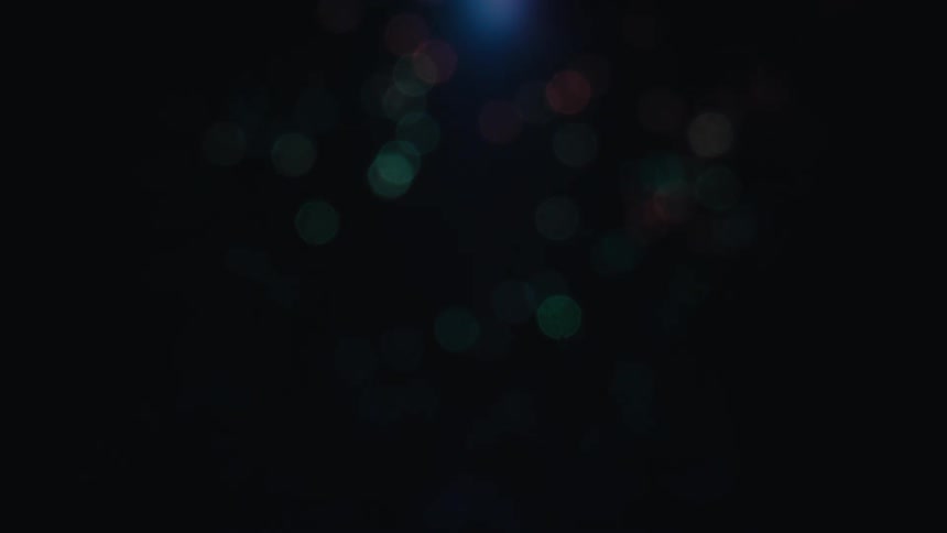 Abstract out of focus light particles shift colors and intensity against a black background
