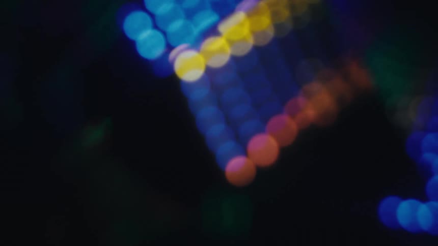 Out of focus colorful lights move across a dark background